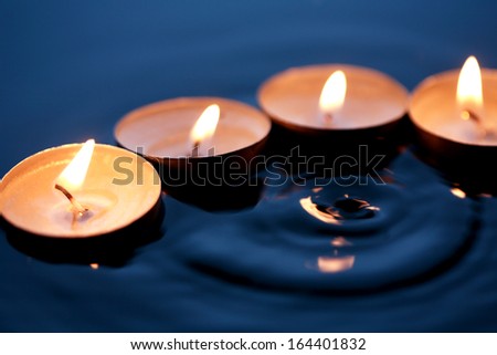 Few lighting candles on dark splashing water surface