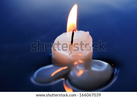 One lighting candle on calm blue water