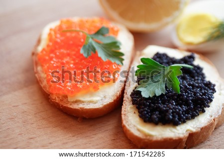 Two sandwiches with red and black caviar on wooden board near lemon and egg