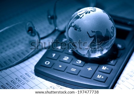 Business concept. Glass globe on calculator near spectacles on background with table of numbers
