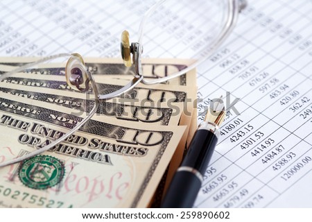 Bookkeeping concept. Closeup of eyeglasses and pen near dollar bank notes on paper list with digits