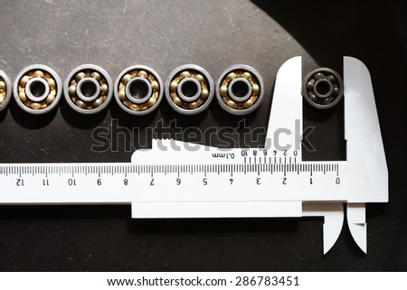 Set of few ball bearings and caliper on dark metal background