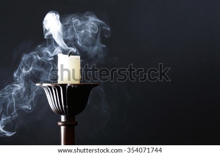 Extinguished candle in candlestick with smoke on dark background