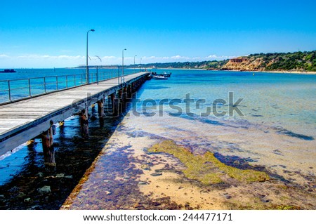 Wooden pier stretches out into clear blue water on an Australian beach