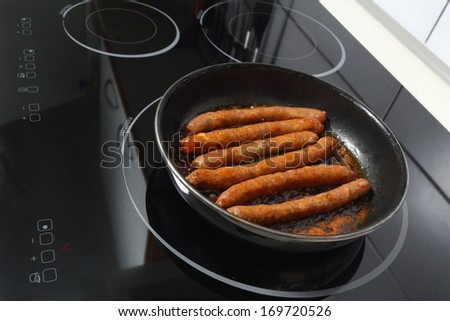Details of merguez sausages baking in a frying pan on ceramic hob.
