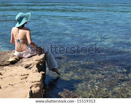 Woman wearing white linen pants sitting on the shore of Adriatic sea. Croatia.