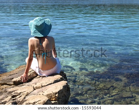Woman wearing white linen pants sitting on the shore of Adriatic sea. Croatia.