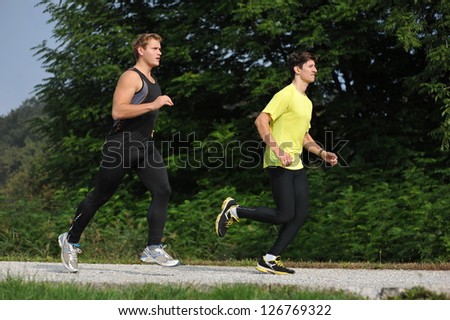 Two Men Athletes Running Through Park