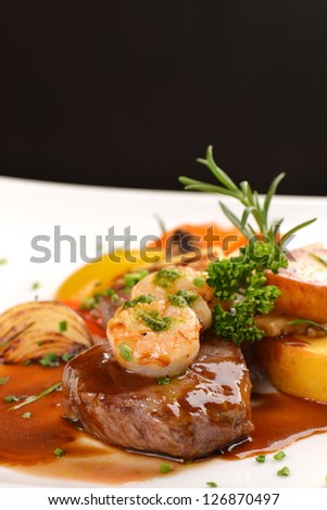 Delicious juicy barbecued steak and prawns with grilled tomato and roasted potatoes. Surf and Turf style. Shallow dof