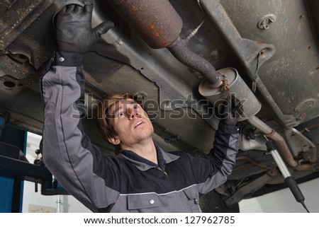 Car mechanic repairs exhaust system