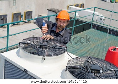 Air Conditioning Repair, repairman on the roof fixing huge air conditioning system. Model is actual electrician.