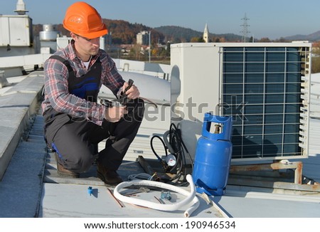 Air Conditioning Repair, young repairman on the roof fixing air conditioning system. Model is actual repairman / electrician.