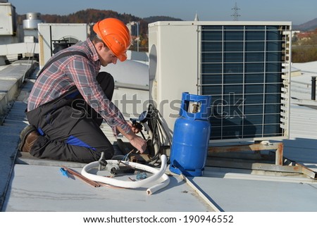 Air Conditioning Repair, young repairman on the roof fixing air conditioning system. Model is actual repairman / electrician.