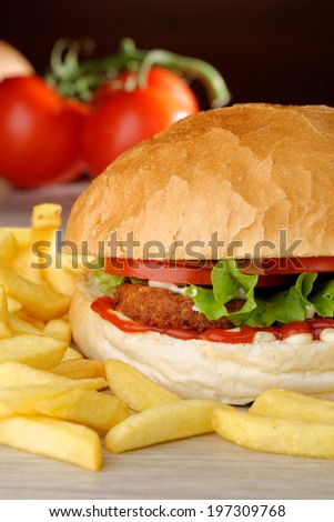 Big vegetarian burger with lettuce, tomato and cucumber accompanied by French fries (Selective Focus, Focus on the front of the lettuce, lentil burger, tomato and sauces)