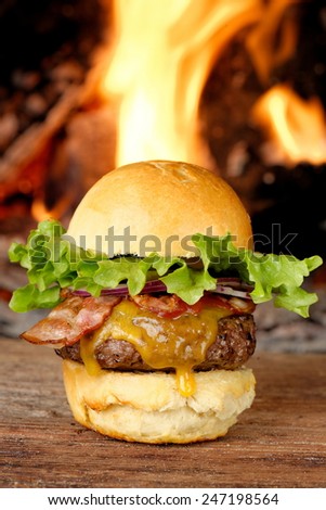 Gourmet bacon cheeseburger with lettuce and tomato in front of the fire
