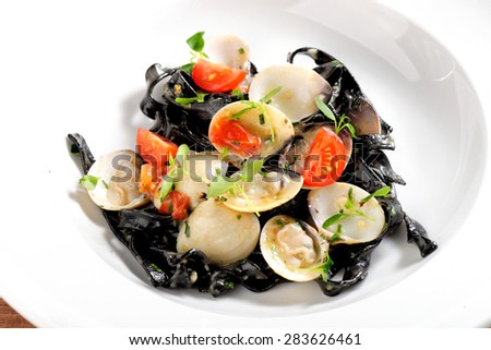 Close-up of squid ink colored tagliatelle with sliced octopus and vongole mussels