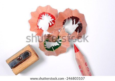 Bright red pencil with knife-sharpener and color wood shavings on a white background