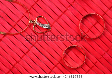 Two gold wedding rings and gold heart with chain on the red bamboo surface