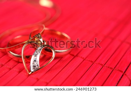 Two gold wedding rings and gold heart with chain on the red bamboo surface
