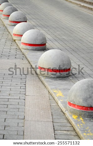 Round stone road kerb with a red strip standing in a row and on a diagonal on a paving stone.