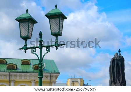Streetlight against the blue sky and a monument to the priest.