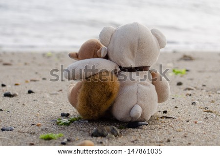 Stuffed animals sitting in the sand looking at the ocean