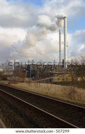 The chimney of a factory with white smoke near railway