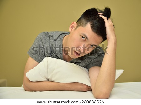 Thai man holding his pillow on his bed with the yellow background. Good for health topic that require a relaxing photo.