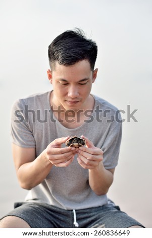 Thai young man holding a thai snail-eating turtle in his both hands with an interesting face.