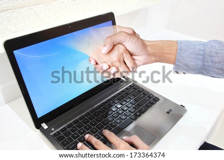 Business man hand reaching out from screen laptop to shake Hand from notebook pc.