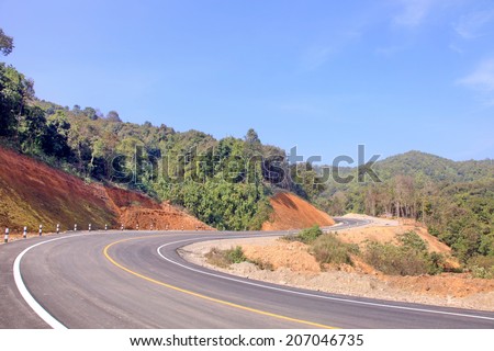 The country road in the mountains curve as an arrow on the background forest