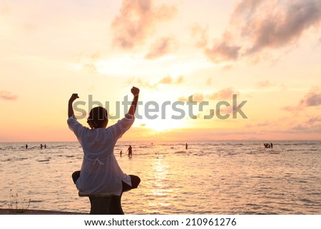 Happy celebrating winning success woman at sunset or sunrise seatting elated with arms raised up above her head in celebration of having reached mountain top summit goal during hiking travel trek.