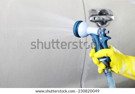 Hand in yellow glove grip nozzle spray squirting said a white car.