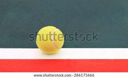 Tennis ball on green painted white line and the floor outside the red zone.