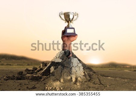 Gold trophy for champion cup, Dirty hands holding the cup holds up through the asphalt road surface.\
The concept Must contend with numerous obstacles to obtain victory.