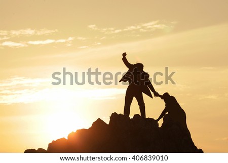 Silhouette of the man Bring hand up a friend to top the peak of mountain on sunrise sky , Business success goal together, Conceptual design.