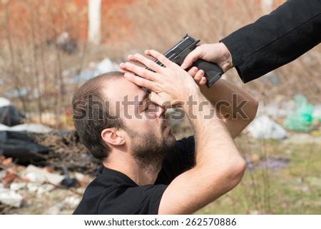 Male hand with black sleeve pointing gun on male head
