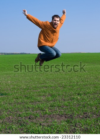 Jumping man in jeans and orange jacket on blue sky and green grass background