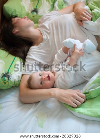 Awake baby with sleeping mom in a bed