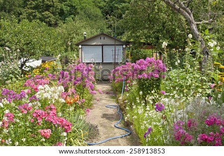 beautiful cottage garden scene with a little garden house, a path & lots of flowers and trees.