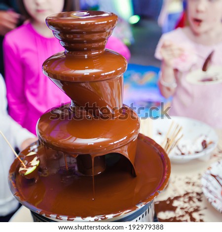 Vibrant Picture of Chocolate Fountain Fontain on childen kids birthday party with a kids  playing around and marshmallows and fruits dip dipping into fountain