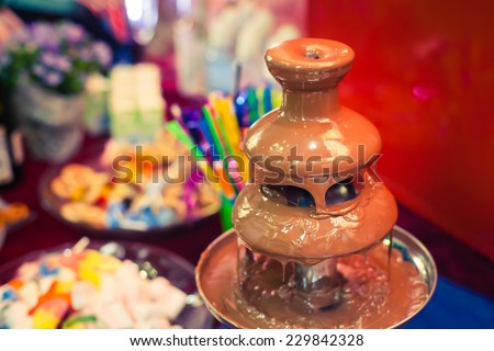 Vibrant Picture of Chocolate Fountain Fontain on childen kids birthday party with a kids playing around and marshmallows and fruits dip dipping into fountain