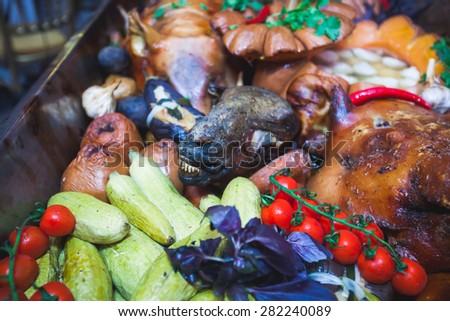 Big dish plate with roasted full pork head, served in restaurant with vegetables, lamb, ham and chicken.