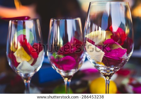 Beautiful glass with rose leafs, rose-petal, rose petals on a romantic date with wine, candles in candlelight and with celebrating couple on the background, interior for a romantic date diner