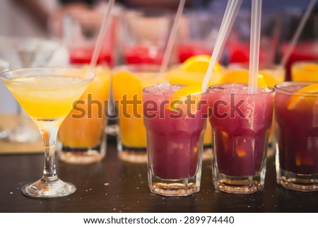 Beautiful line of different colored alcohol mojito cocktails with mint on a open air party, tequila, martini, vodka, and others on decorated catering bouquet table on open air event party