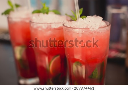 Beautiful line of different colored alcohol mojito cocktails with mint on a open air party, tequila, martini, vodka, and others on decorated catering bouquet table on open air event party