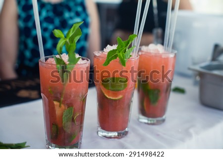 Beautiful line of different colored alcohol mojito cocktails with mint on a open air party, tequila, martini, vodka, and others on decorated catering bouquet table on open air event corporate party