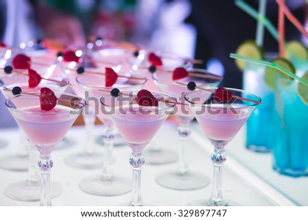 Beautiful row line of different colored alcohol cocktails with mint on a open air party, martini, vodka with bubbles,and others on decorated catering bouquet wedding table on open air event, in night