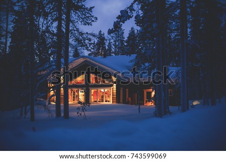A cozy wooden cabin cottage chalet house covered in snow near ski resort in winter with the lights turn on, evening picture