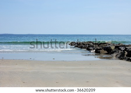 Beautiful shot of the ocean with the tide, the beach, and rocky shore.